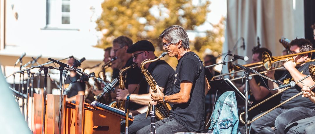 Eine Outdoor-Aufführung einer Jazzband. Ein Mann spielt Saxophon. Ein Lautsprecher steht vor ihm.