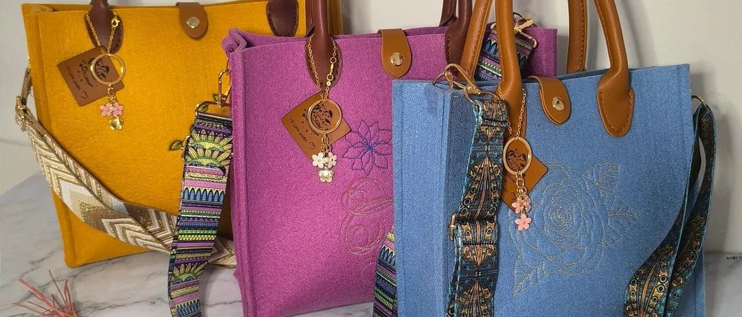 Vier Handtaschen in verschiedenen Farben sind auf einer Marmoroberfläche ausgestellt. Die gelbe, lila und blaue Tasche haben dekorative Riemen und Anhänger.