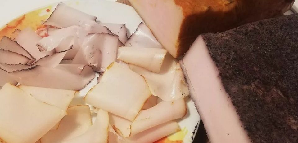 Ein Teller mit dünn geschnittenem Fleisch und zwei großen Scheiben gepökelten Fleisches auf Holzbrettern. Der Teller hat ein farbenfrohes Design.