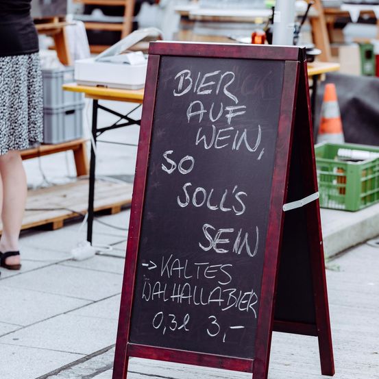 Ein Kreidetafel-Schild mit weißer Schrift. Es steht: 'BIER AUF WEIN, SO WEIN SOLLS SEIN'. Darunter steht ein Hinweis, der lautet: 'Kaltes Wahlhallbier 0,3l 3-'.