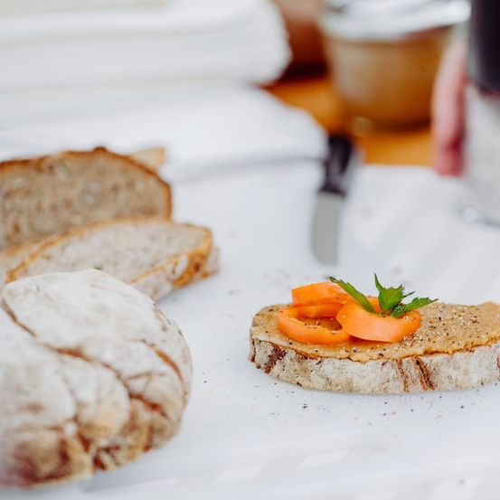 Ein Stück Vollkornbrot mit einer Schicht Aufstrich und belegt mit dünnen Karottenscheiben und einer Petersilie.