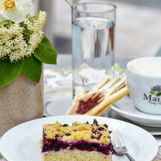 Ein Tisch mit einem Dessert, einer Tasse Kaffee, einem Glas Wasser und einer Vase mit Blumen.