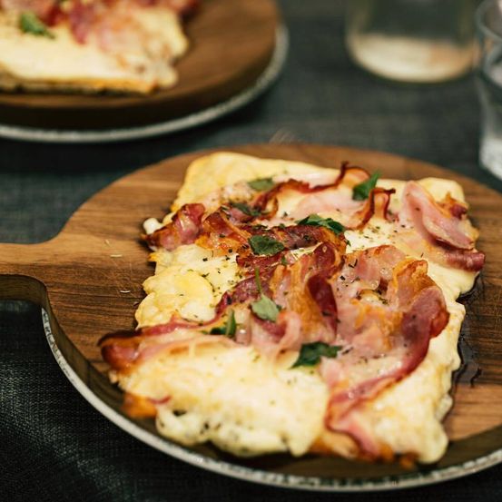 Ein Holzteller mit einer Scheibe Pizza, belegt mit geschmolzenem Käse, knusprigem Speck und Kräutern.