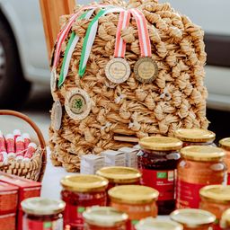 Eine Ausstellung von Honigprodukten mit Gläsern und einem Korb mit Lippenbalsam. Im Hintergrund befindet sich ein gewebter Honigwabenbeutel mit Medaillen.