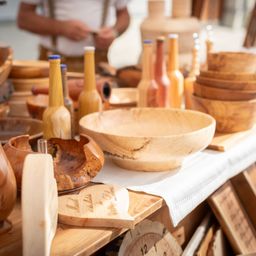 Eine Vielzahl von Holzschüsseln, Flaschen und Utensilien sind auf einem Tisch mit einem weißen Tuch angeordnet. Eine Person steht hinter dem Tisch, möglicherweise in Vorbereitung auf eine Veranstaltung.