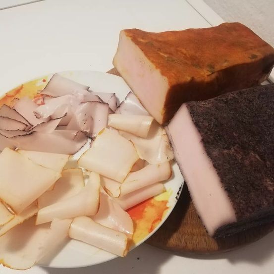 Ein Teller mit geschnittenem Schinken und zwei Arten von Wurst auf einem hölzernen Schneidebrett.