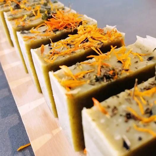 Eine Reihe handgefertigter Seifenstücke mit orangefarbenen Blumen und Kräutern darauf liegt auf einer Holzoberfläche.