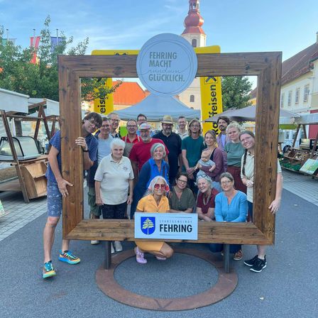 Eine Gruppe von Menschen posiert vor einem Schild, das 'Fehring Macht Glucklich' in einer Fotokabine sagt.