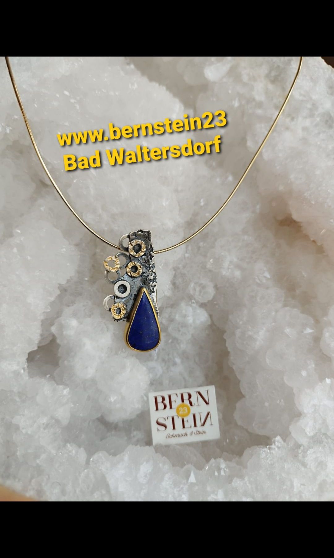 Eine goldene Halskette mit einem blauen Lapis-Lazuli-Anhänger ruht auf einem Bett aus weißen Salzkristallen. Der Anhänger besteht aus einem blauen Edelstein mit aufwendigen Verzierungen darum.