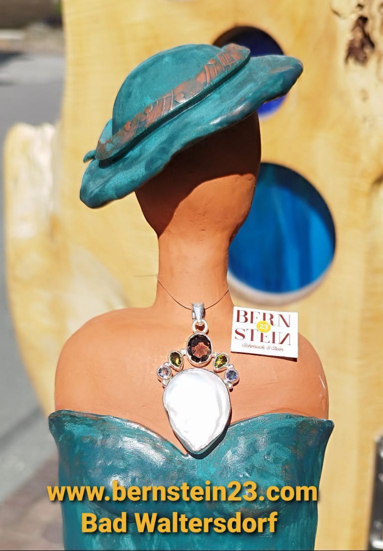 Eine Mannequin-Büste mit einem türkisfarbenen Hut und einer Halskette mit einer großen weißen Perle und mehrfarbigen Edelsteinen. Die Kette hat einen Anhänger, der 'BERN STEIN' besagt.