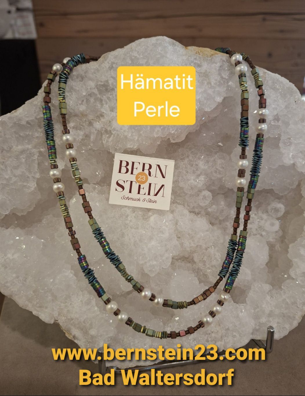 A double-layered necklace made of green and brown beads with white pearls, resting on a large crystal rock. The necklace has a yellow label with the text 'BERN STEIN'.