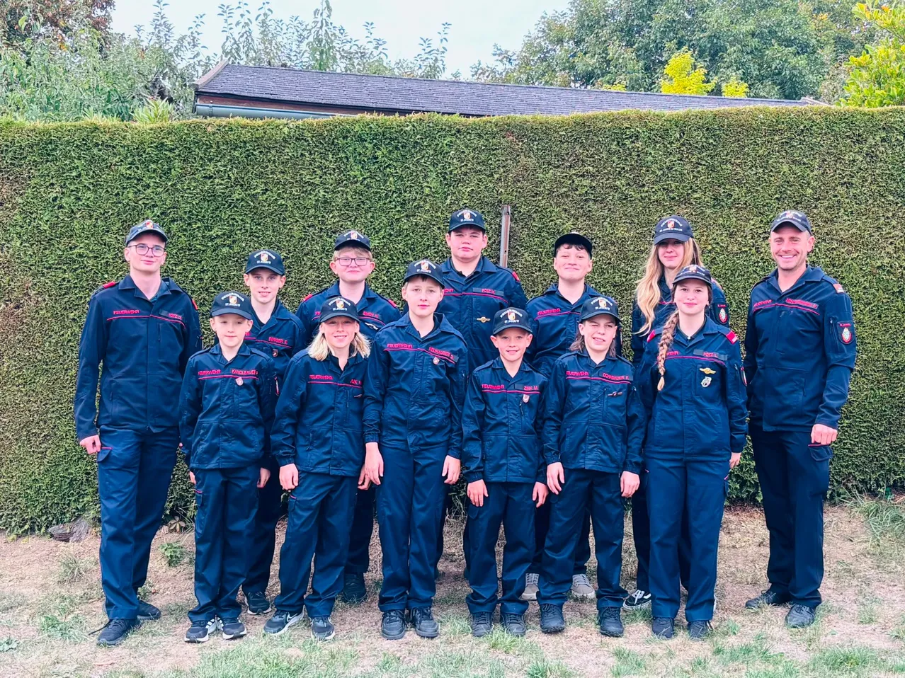 Eine Gruppe von Menschen in blauen Uniformen posiert für ein Foto vor einer Hecke.