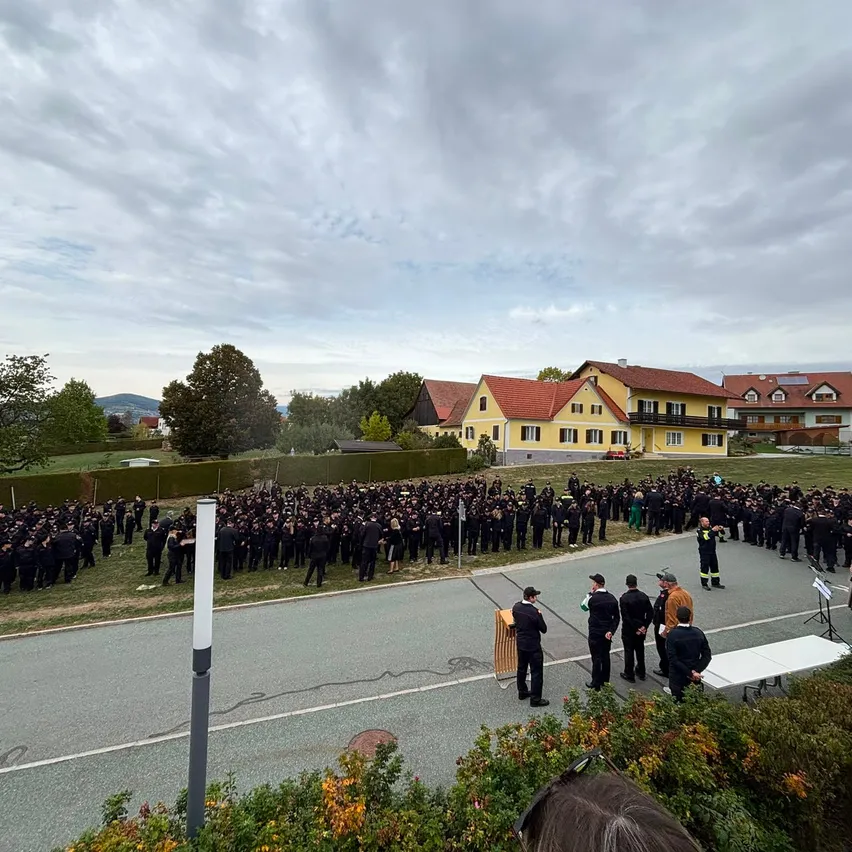 Eine große Gruppe von Menschen in Uniform steht in einer Reihe am Straßenrand, mit einem gelben Gebäude im Hintergrund.