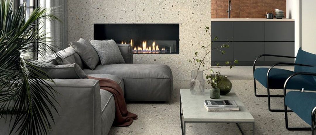 Ein modernes Wohnzimmer mit Kamin, grauem Sofa und einem Tisch mit Pflanzen. Die Küche ist im Hintergrund zu sehen.