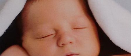 Ein Baby schläft friedlich unter einer Decke und sieht mit geschlossenen Augen und einem leichten Lächeln friedlich aus.