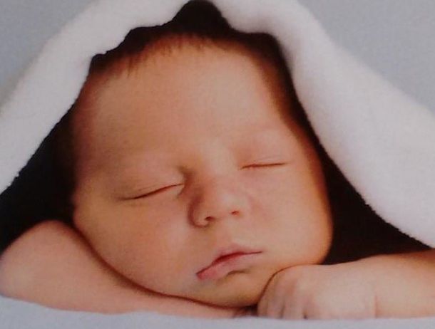 Ein Baby schläft friedlich unter einer Decke und sieht mit geschlossenen Augen und einem leichten Lächeln friedlich aus.