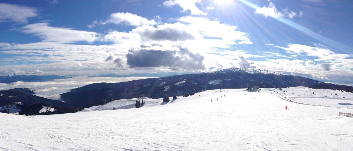 Verschneite Berghänge mit Skifahrern an einem sonnigen Tag. Ein klarer blauer Himmel mit ein paar Wolken.