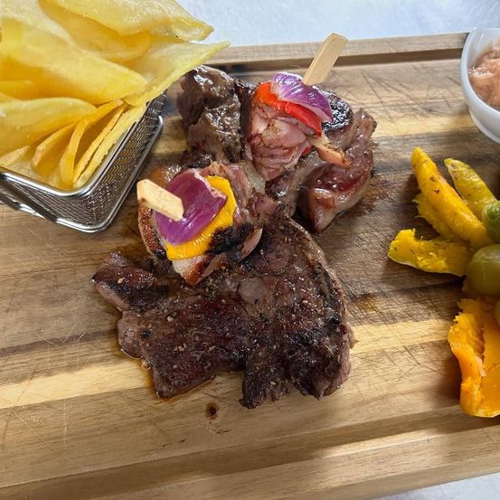 Gegrilltes Steak mit Zwiebeln und Paprika auf einem Holzbrett, neben Pommes und einer Dipschale.
