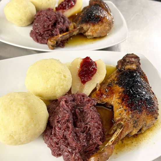 Zwei Teller mit gebratenem Fleisch, Knödeln und Rotkohl. Ein Teller hat ein Bein mit Knochen und der andere hat ein Bein ohne Knochen.