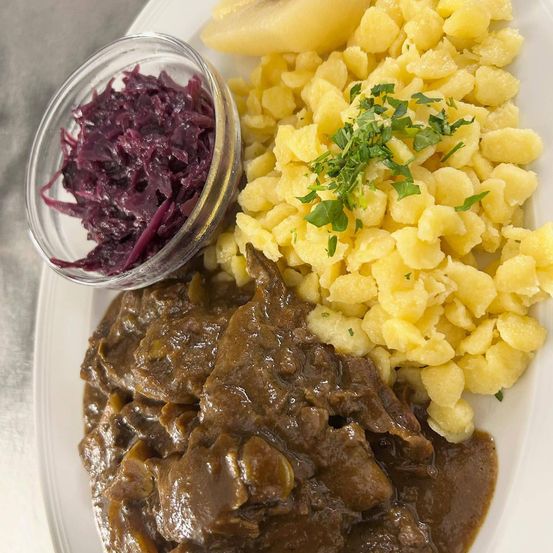 Ein Teller mit gebratenem Rindfleisch in Sauce, Kartoffelpüree und Rotkohl. Das Gericht ist auf einem weißen Teller serviert.
