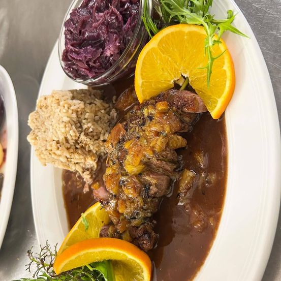Ein Teller mit Fleisch in Soße, Orangenscheiben, Reis und einer Beilage aus Rotkohl.