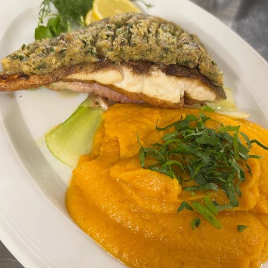 Ein Teller mit einem panierten Fischfilet, begleitet von einer Karottenpüree und mit grünen Kräutern garniert.