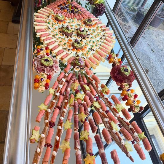 Ein Buffettisch mit verschiedenen Fleisch- und Gemüserollen, verziert mit Sternen und kleinen Früchten, auf einer glänzenden Metalloberfläche.