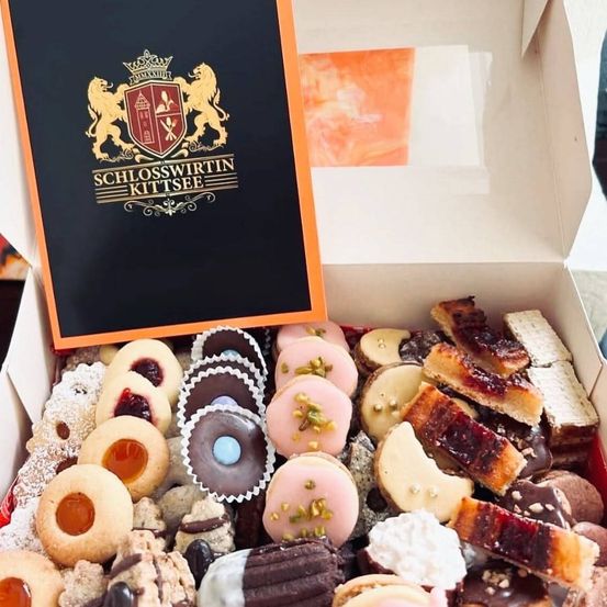Eine Schachtel mit verschiedenen Keksen und Gebäck von Schlosswirtin Kitzsee. Die Schachtel ist geöffnet und zeigt verschiedene Arten von Süßigkeiten, darunter Schokoladen, Macarons und Biscottis.