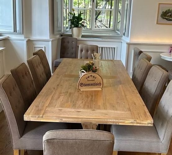 Ein Essbereich mit einem großen Holztisch, Stühlen, einem Topf mit Pflanzen, einer Speisekarte und gerahmter Kunst. Der Tisch hat ein Schild, das Stammtisch steht.