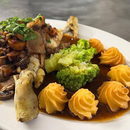 Ein weißer Teller mit einem Gericht bestehend aus Hähnchen, Pilzen, Brokkoli und spiralförmigen Kartoffeln in einer reichhaltigen Sauce.