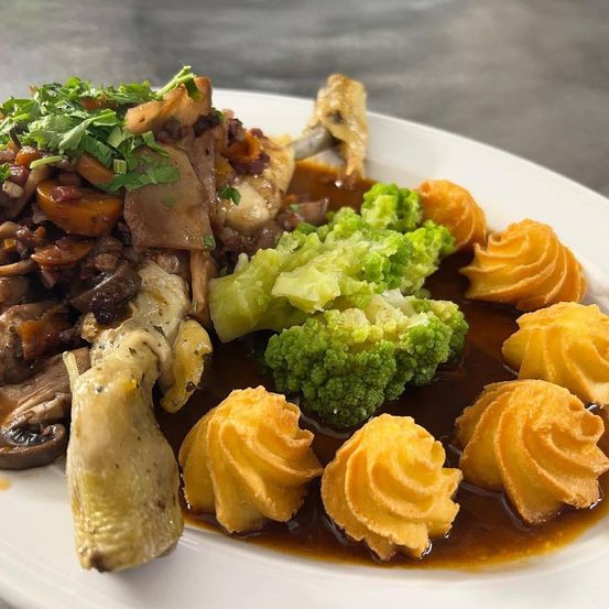 Ein weißer Teller mit einem Gericht bestehend aus Hähnchen, Pilzen, Brokkoli und spiralförmigen Kartoffeln in einer reichhaltigen Sauce.
