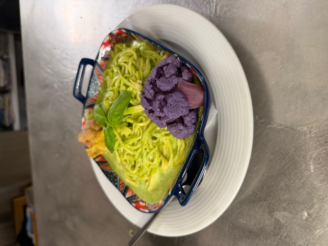 Eine Schüssel grüner Pasta mit violettem Blumenkohl und Basilikum auf einem weißen Teller.