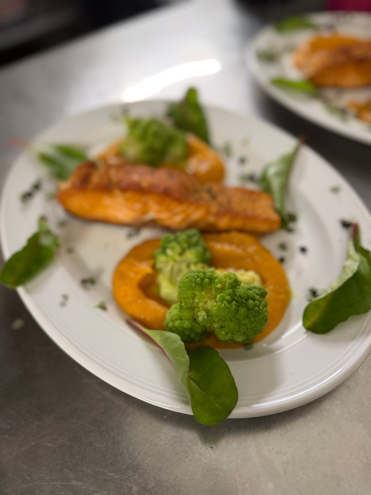 Ein weißer Teller mit Lachs und Brokkoli auf einem Tisch.