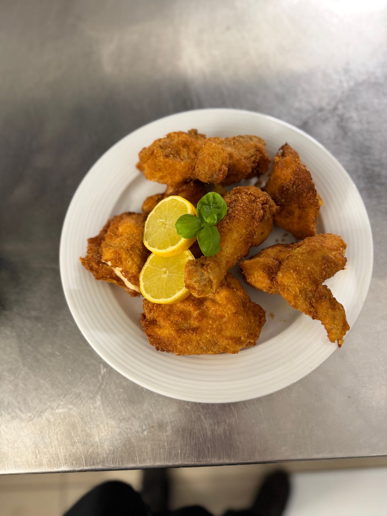Ein weißer Teller enthält gebratene Hühnchenstücke mit zwei Zitronenscheiben und Basilikumblättern obenauf.
