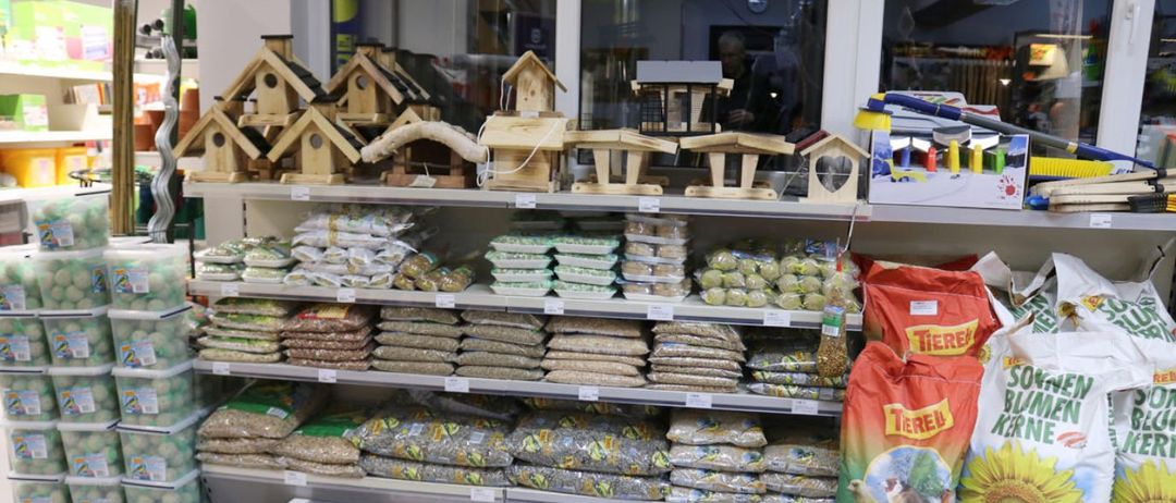 Ein Geschäft gefüllt mit Vogelhäusern und verschiedenen Vogelfuttersorten auf Regalen, mit einem Beutel Vogelfutter vorn.