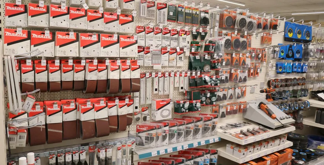 Ein Geschäft mit verschiedenen Makita-Produkten zur Ausstellung, einschließlich Werkzeuge und Zubehör, ordentlich auf Regalen und Tafeln organisiert.