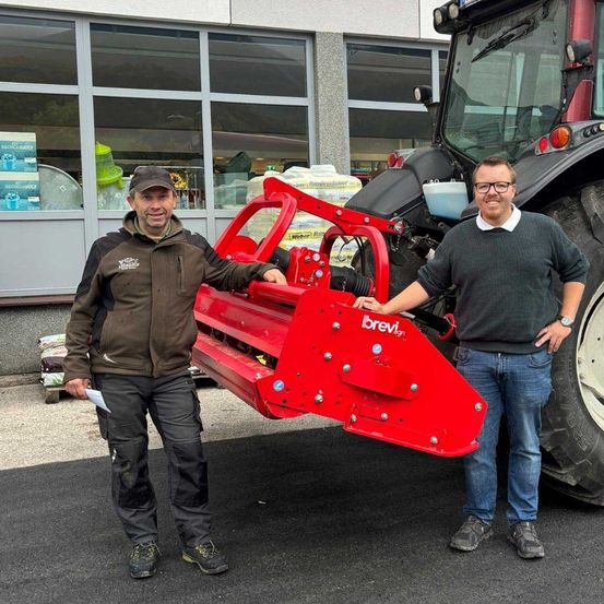 Zwei Männer stehen neben einem roten Traktor. Ein Mann hält den vorderen Teil des Traktors. Sie lächeln beide.