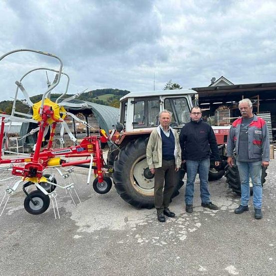 Drei Männer stehen vor einem großen roten Traktor und einer roten landwirtschaftlichen Maschinerie. Sie tragen alle Winterkleidung.