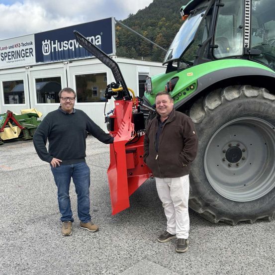 Zwei Männer stehen neben einem Traktor vor einem Gebäude mit einem Schild, das 'Husqvarna' besagt.