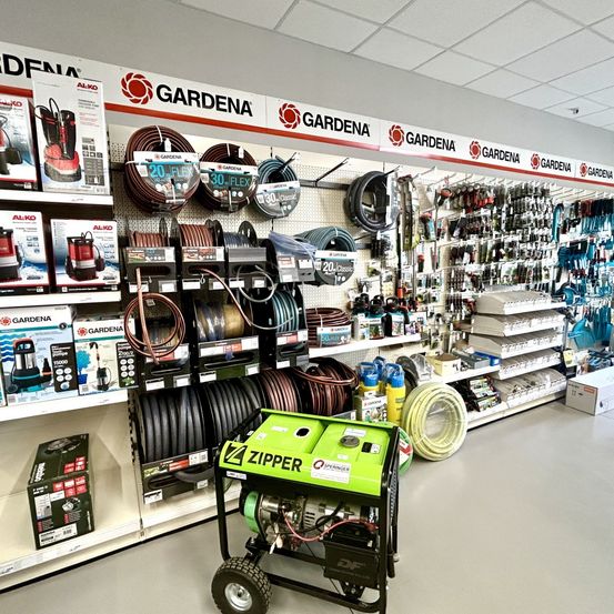 Ein Geschäft gefüllt mit Gartengeräten, mit einer prominenten Präsentation von GARDENA-Produkten, einschließlich eines grünen Generators, verschiedener Schläuche und Werkzeuge.