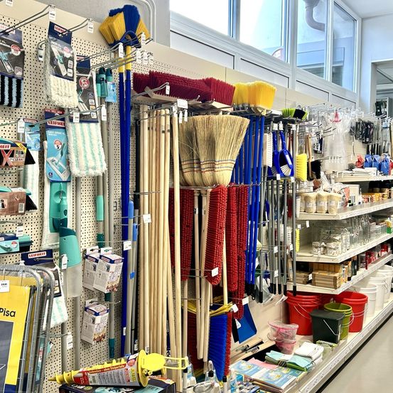 Ein Ladengang mit verschiedenen Reinigungswerkzeugen und -utensilien, einschließlich Besen, Kehrbleche und Reinigungslösungen. Die Produkte sind ordentlich auf Regalen und Haken angeordnet.