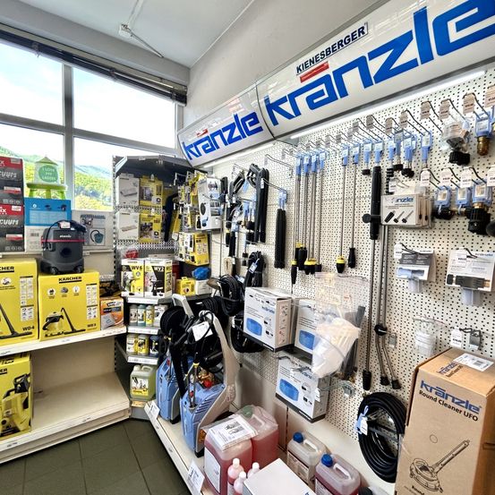 Ein Ladeninneres mit einem Kranzle-Banner, verschiedenen Reinigungsgeräten und Produkten auf Regalen, einschließlich Karcher-Staubsaugern und anderer Reinigungswerkzeuge.
