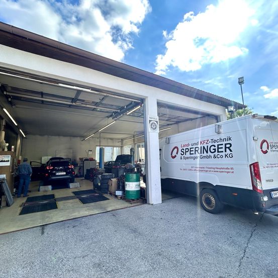 Ein weißer Van mit der Aufschrift 'Land- und KFZ-Technik Speringer & Speringer GmbH & Co KG' vor einer Garage mit einem Auto im Inneren.