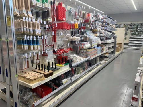 Ein Ladengang gefüllt mit verschiedenen Mal- und Reinigungswerkzeugen, einschließlich Pinsel, Walzen und Dosen, die ordentlich auf Regalen und Metallhakentafeln angeordnet sind.