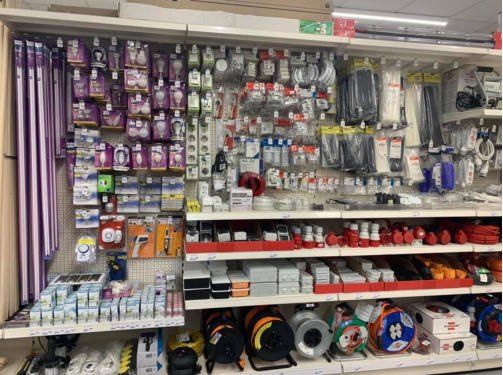 Ein Geschäft mit vielen Regalen, die mit verschiedenen Produkten wie Beleuchtung, Verkabelung und elektrischem Zubehör gefüllt sind. Jedes Regal hat ordentlich angeordnete Artikel, einige in bunten Verpackungen.