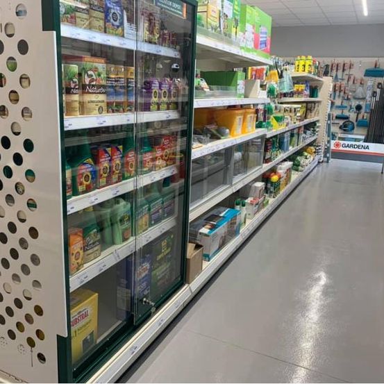 Ein Gang in einem Geschäft mit einer gekühlten Vitrine mit Glasfront und Regalen, die mit verschiedenen Produkten gefüllt sind. Der Laden hat ein sauberes und ordentliches Erscheinungsbild.