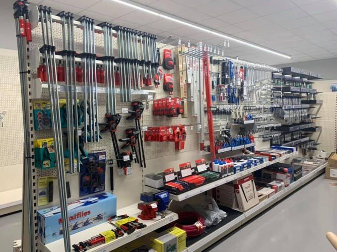 Ein Baumarkt mit verschiedenen Werkzeugen und Geräten, die ordentlich auf Regalen angeordnet sind. Jedes Regal enthält verschiedene Werkzeuge, einige hängen an Hakenbrettern. Es gibt Kisten, Behälter und Container, die Werkzeuge halten. Ein langes Regal beherbergt mehrere Werkzeuge. Eine weiße Deckenleuchte beleuchtet den Bereich.