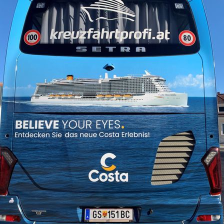 Die Rückseite eines Busses zeigt eine Werbung für ein Kreuzfahrtschiff. Die Anzeige zeigt ein Schiff mit 'Costa Smeralda' darauf und lädt die Betrachter ein, 'Glaube deinen Augen'. Das Design zeigt einen blauen Ozean im Hintergrund und einen Wasserzeichen mit 'kreuzfahrtprofi.at'. Das Kennzeichen lautet 'GS 151 BC'.
