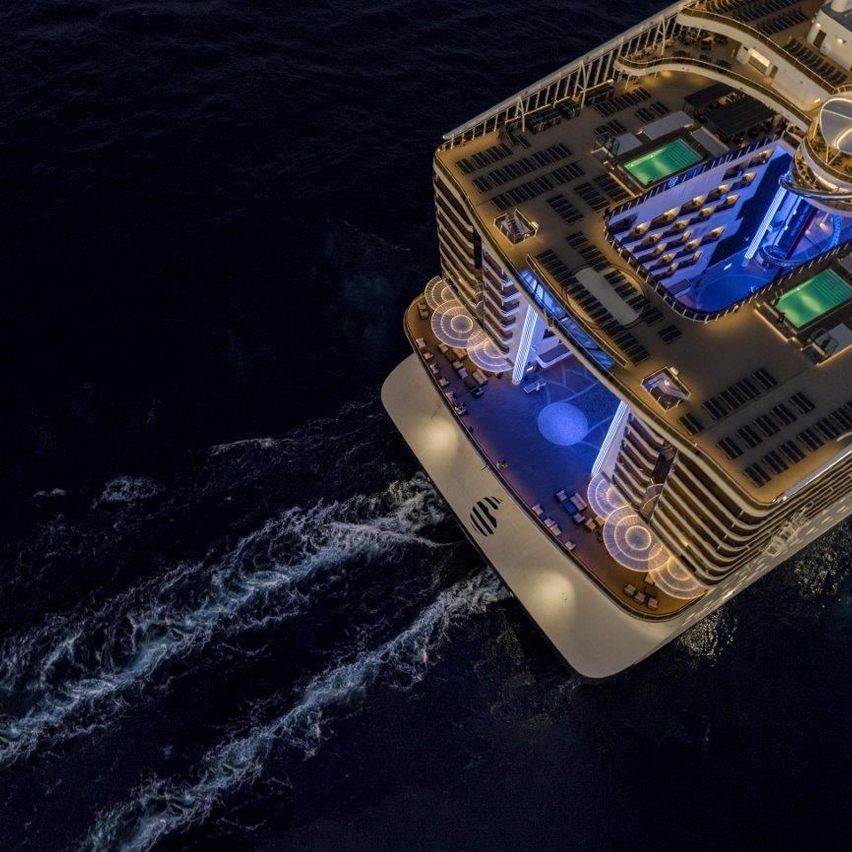 Ein Luftbild eines Luxuskreuzfahrtschiffs mit blauen Lichtern, das bei Nacht auf dunklem Wasser fährt.