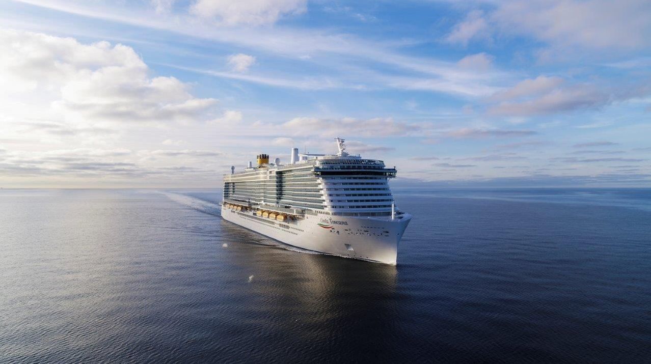 Ein großes weißes Kreuzfahrtschiff, Costa Toscana, segelt auf dem Ozean unter einem blauen Himmel mit verstreuten Wolken.